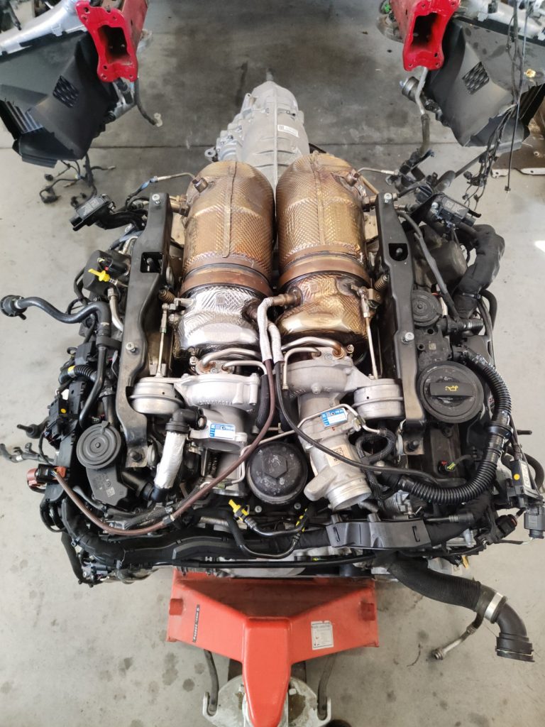 Kompletný motor s dvoma turbami, prevodovkou a výfukovým systémom, položený na červenej palete.