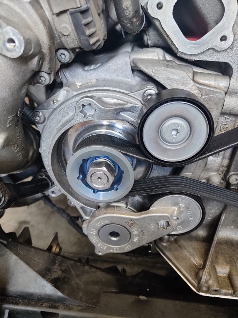 Detailný pohľad na systém rozvodového remeňa, napínaciu kladku a vodnú pumpu v motore.